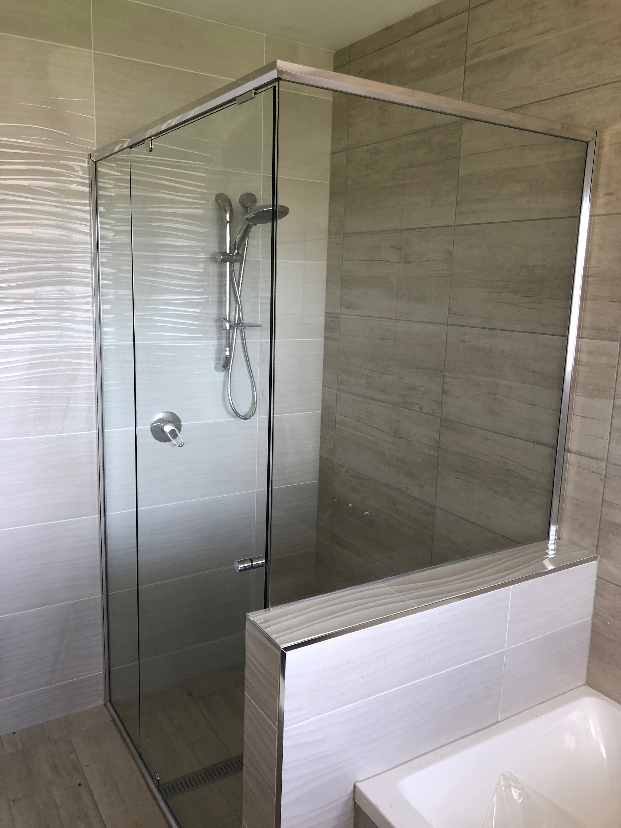Frameless corner shower screen with chrome fittings in a tiled bathroom