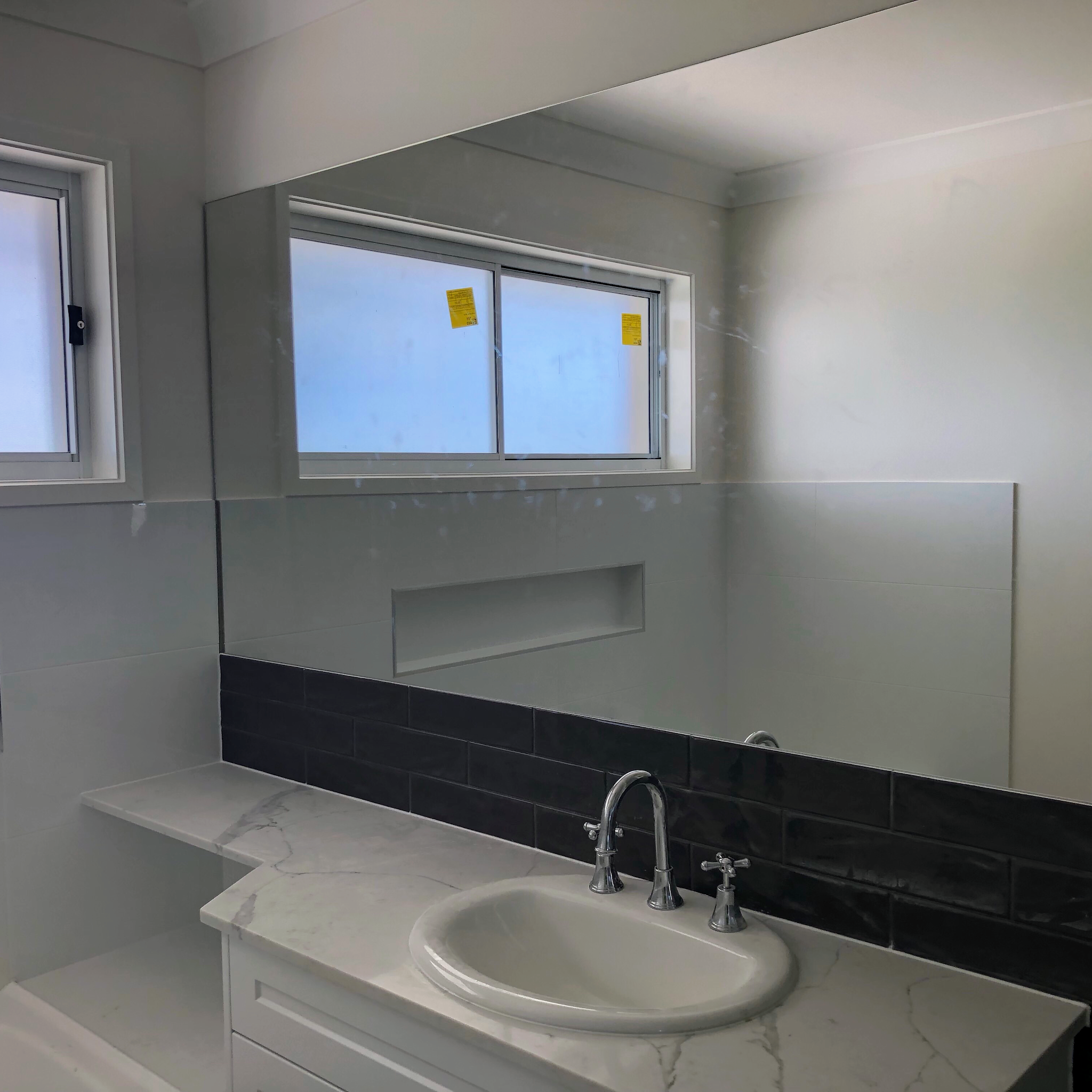 Large bathroom mirror above a marble-look vanity with dark subway tiles