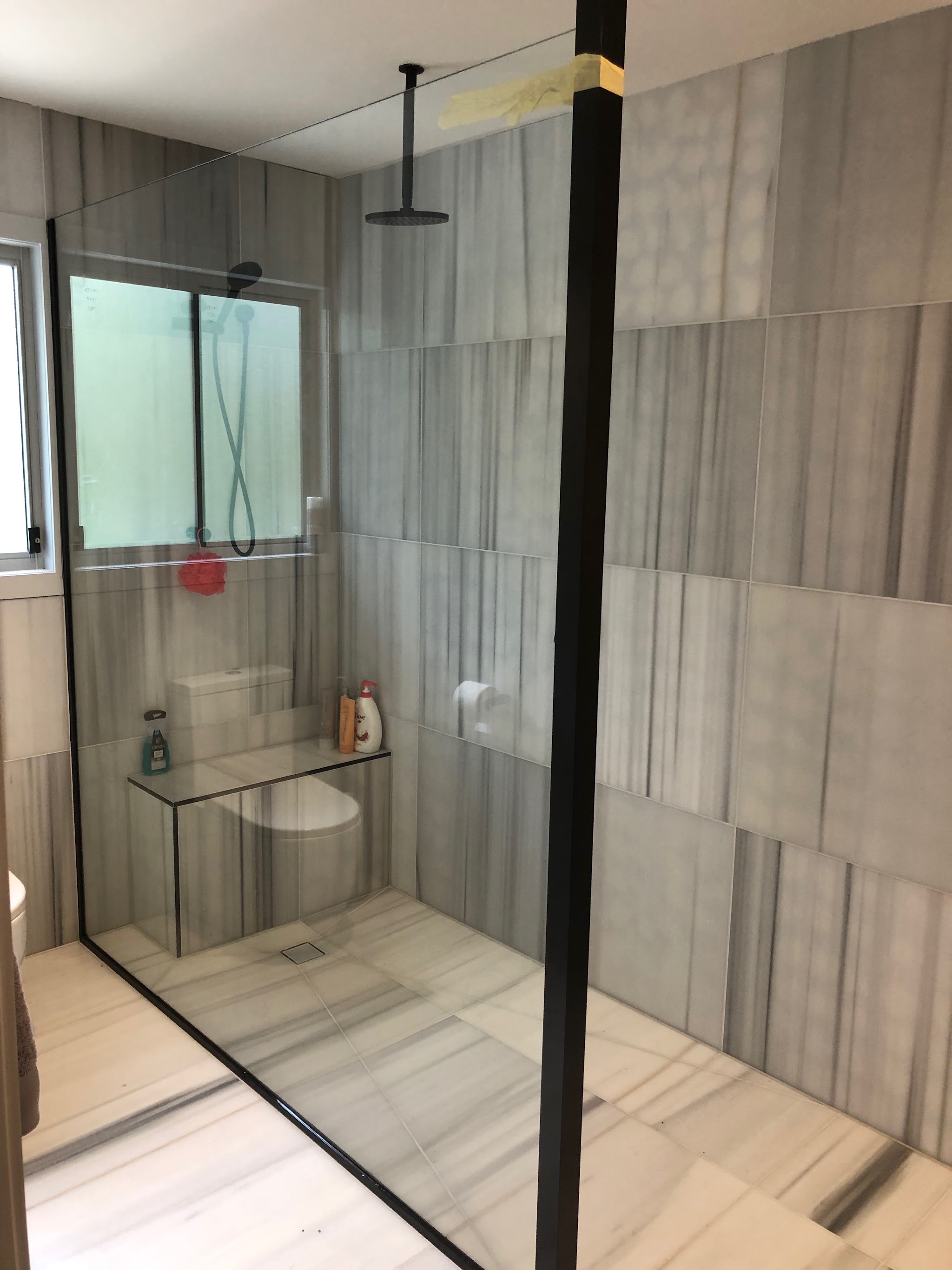Frameless shower screen beside a toilet with grey stone-look tiles